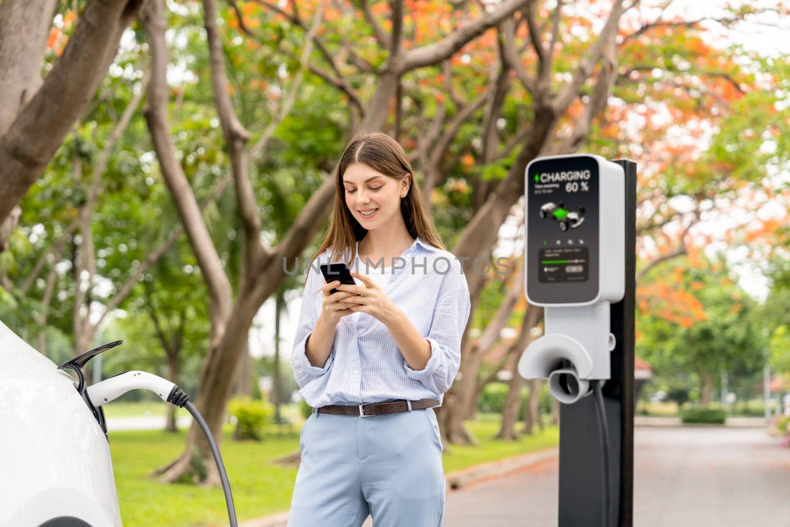 Young woman using smartphone to pay for electric car charging. Exalt by biancoblue