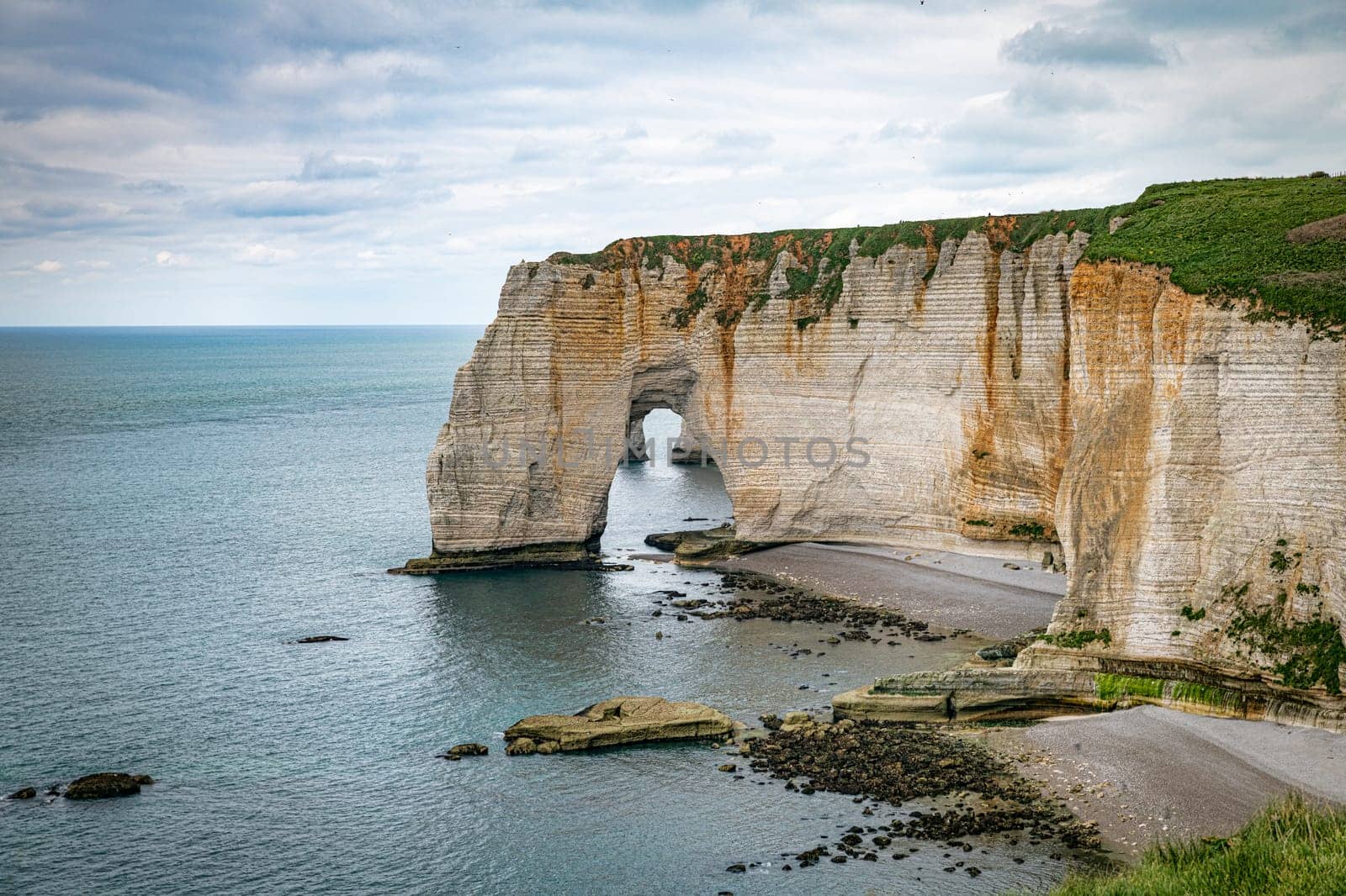 Landscape photo of tall, steep limestone cliffs by the ocean with one with a hole in it creating an arch