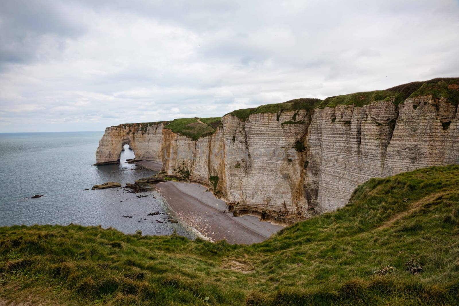 Landscape photo of tall, steep limestone cliffs by the ocean with one with a hole in it creating an arch