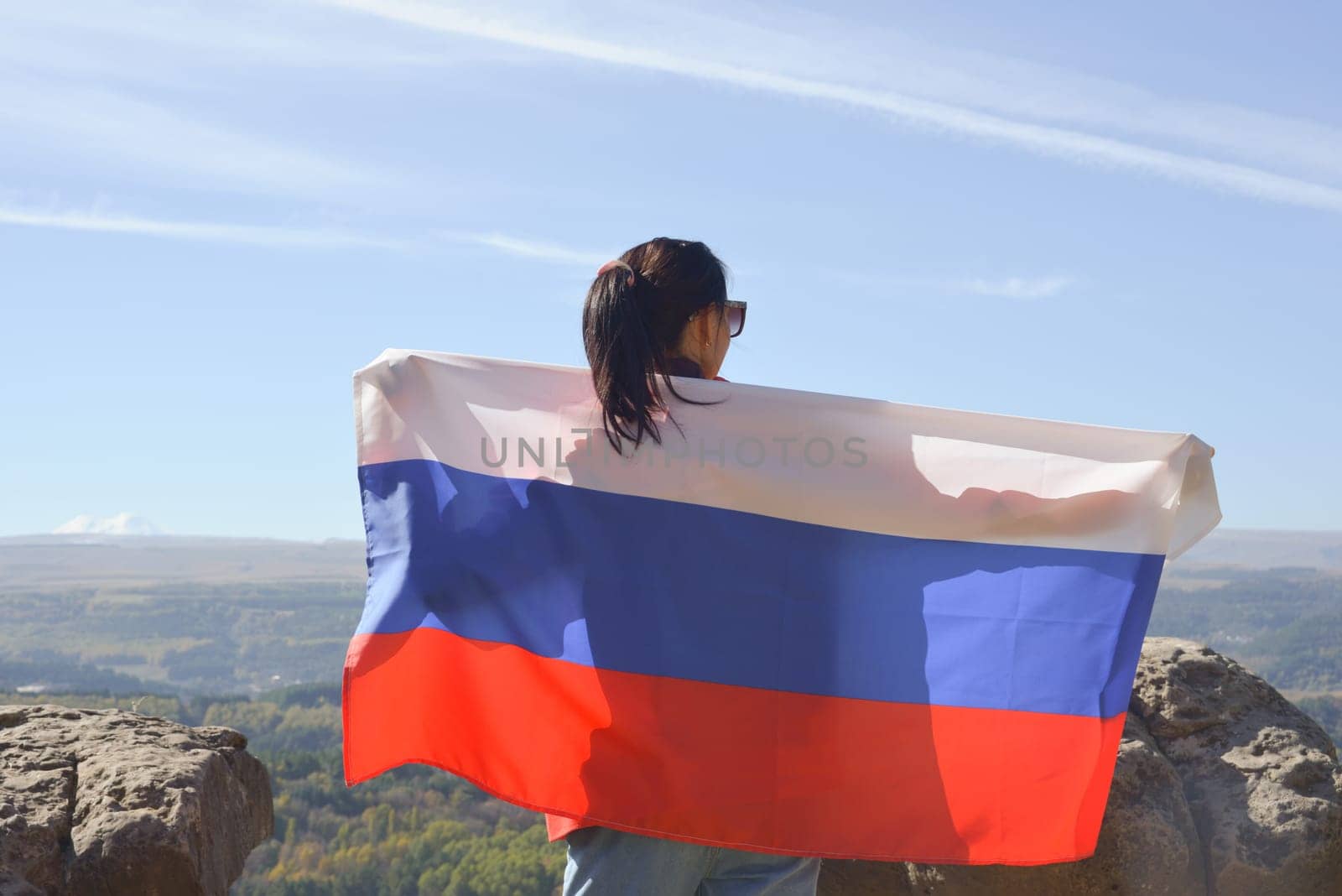 The Russian flag is on the shoulders of a girl standing against the backdrop of the Caucasus mountains. Unity Day in Russia