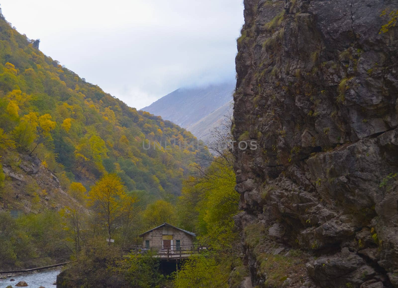A small house near a mountain river and the foot of the misty mountains. North Caucasus, Russia