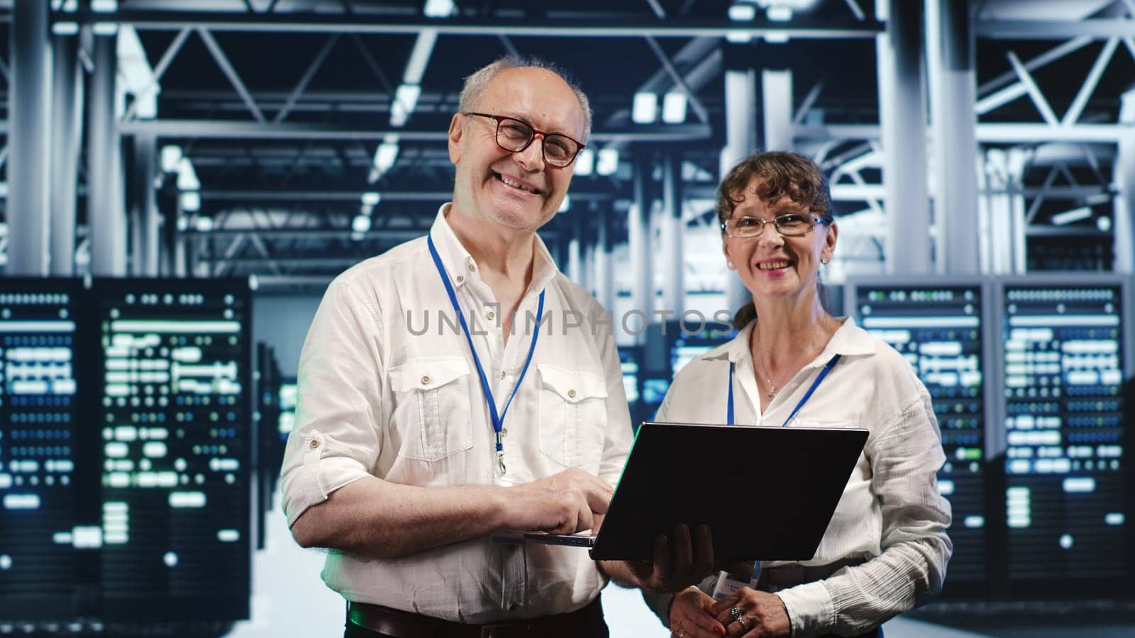 Coworkers in data center using laptop to monitor energy efficient server racks. Equipment using renewable sources employed to minimize consumption and reduce overall facility carbon footprint