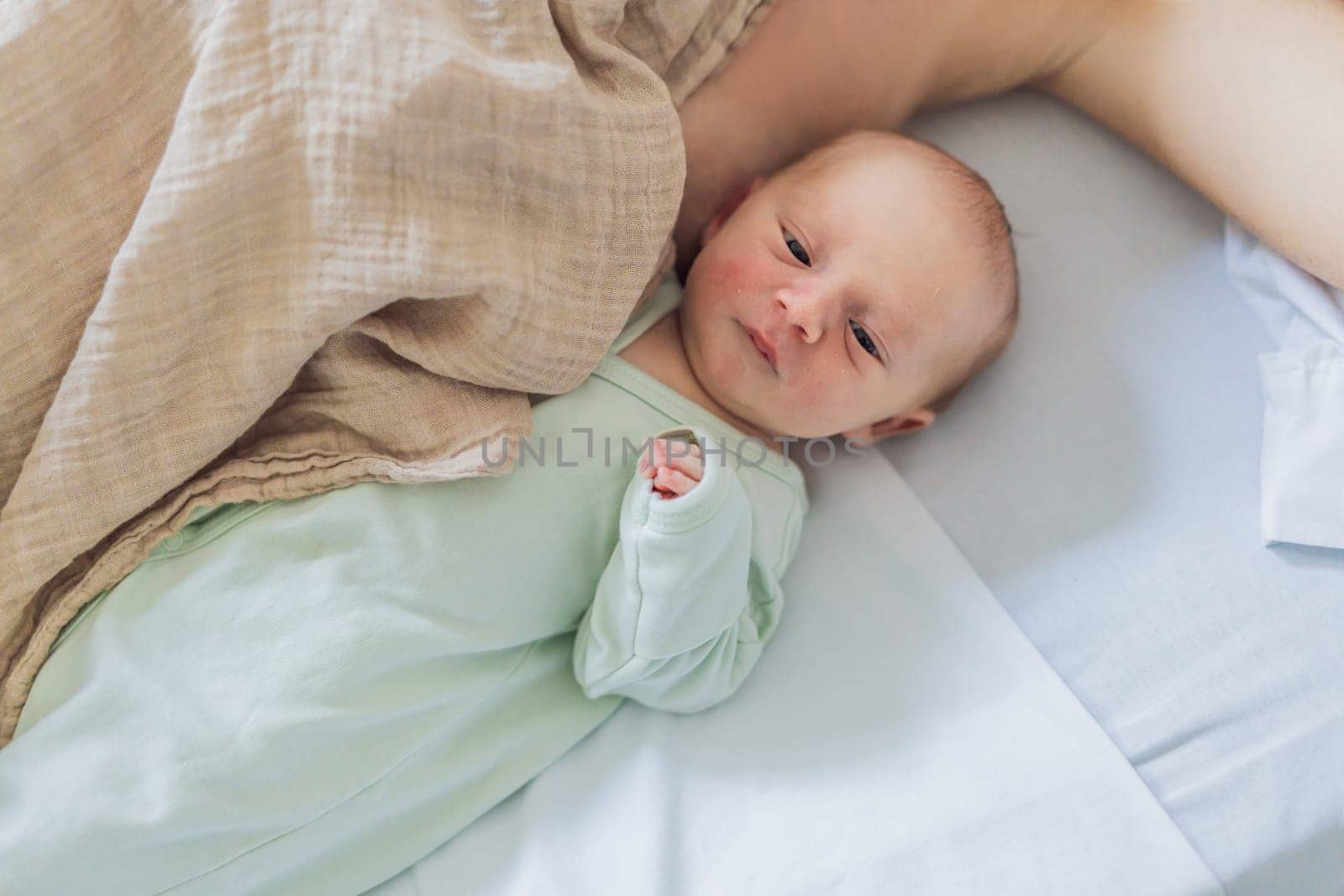 A baby lies with the mother after childbirth, resting peacefully. The serene moment captures the bond between mother and child as they begin their journey together. The hospital environment ensures a safe and comforting space for this intimate interaction.