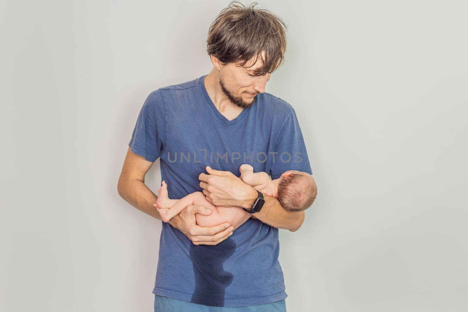 Dad holds newborn and newborn peed on dad. This humorous and heartwarming moment captures the realities of parenting and the bond between father and child in a candid family setting.