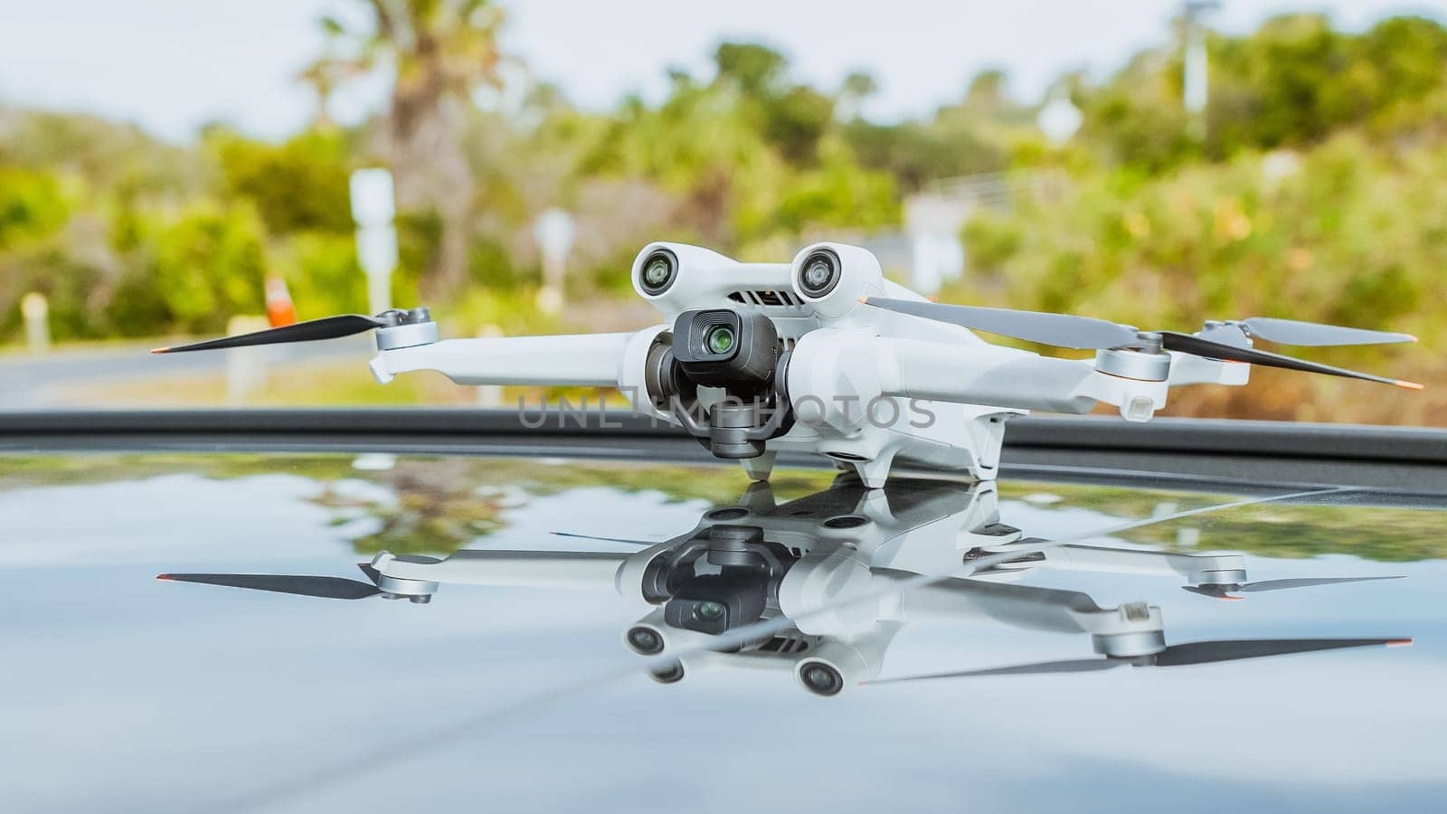 White quadcopter drone with camera on roof of sleek black vehicle parked in urban setting by JuliaDorian