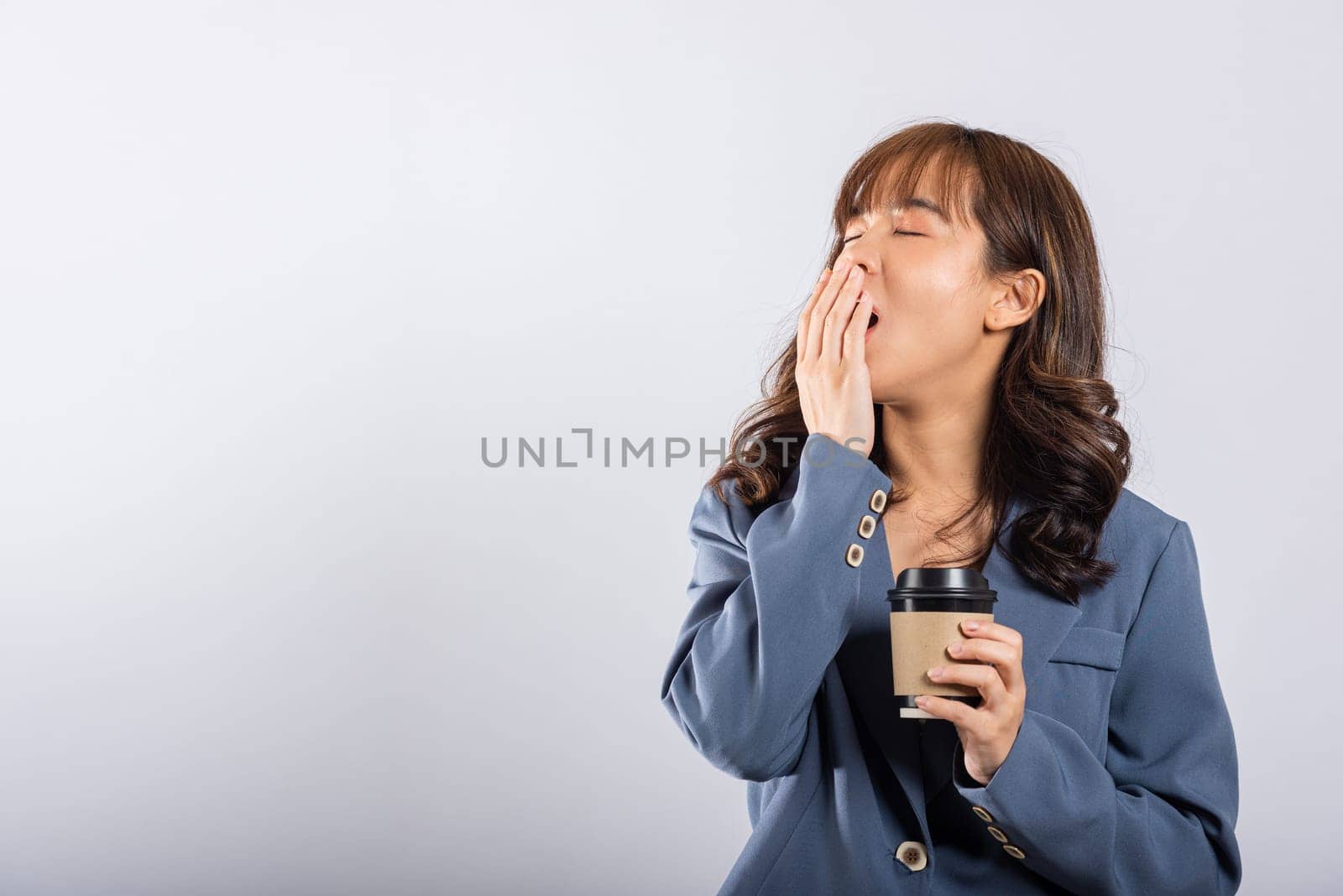 Portrait Asian beautiful business young woman tired sleepy her cannot wake up and closes eyes holds take away cup coffee, studio shot isolated on white background, with copy space by Sorapop