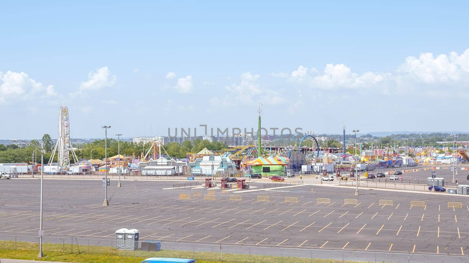 An amusement park with Ferris wheels and roller coasters under a blue sky with white clouds. The rides are colorful and bright. There are a lot of people in the park having fun.