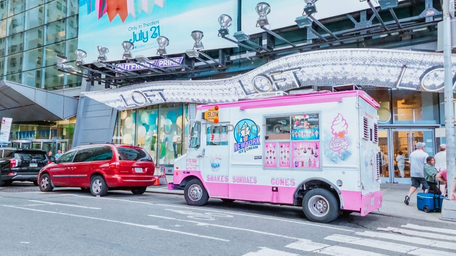 The truck is decorated with colorful lights and has a large sign on the side that says Ice Cream. There are people walking past the truck, and cars are parked on the street behind it.
