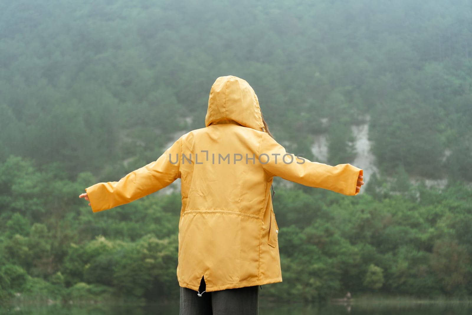 A person in a yellow jacket is standing in the rain, looking up at the sky. Scene is peaceful and serene, as the person seems to be enjoying the moment despite the rain