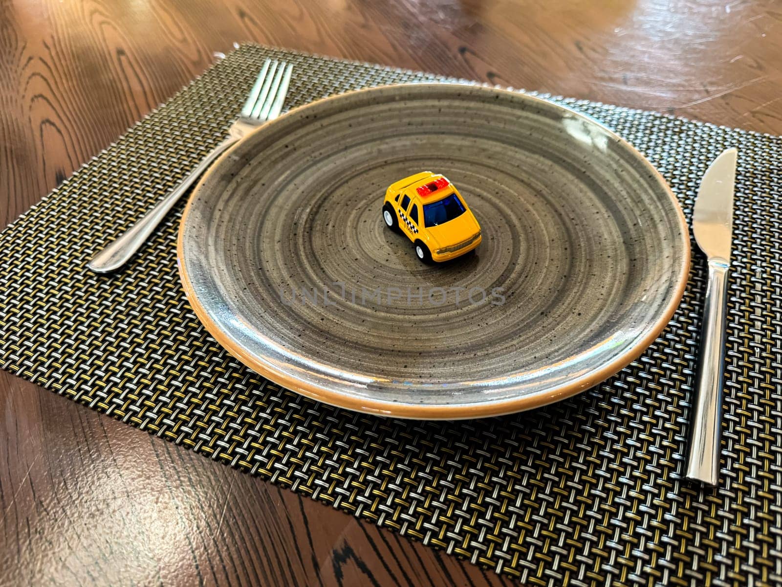 Miniature taxi toy on ceramic plate with cutlery. Concept of calling taxi after end of banquet or celebration. Design of taxi advertising, culinary presentations and unusual concepts. High quality
