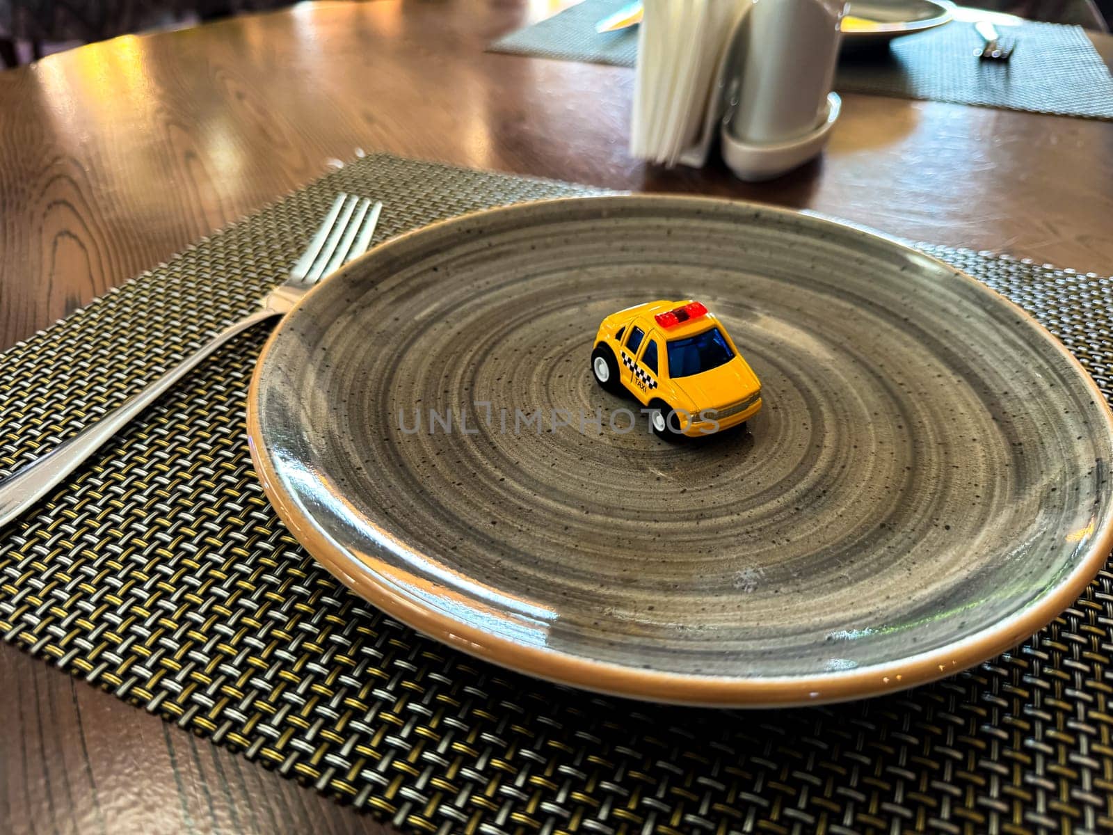 Miniature taxi toy on ceramic plate with cutlery. Concept of calling taxi after end of banquet or celebration. Design of taxi advertising, culinary presentations and unusual concepts. High quality