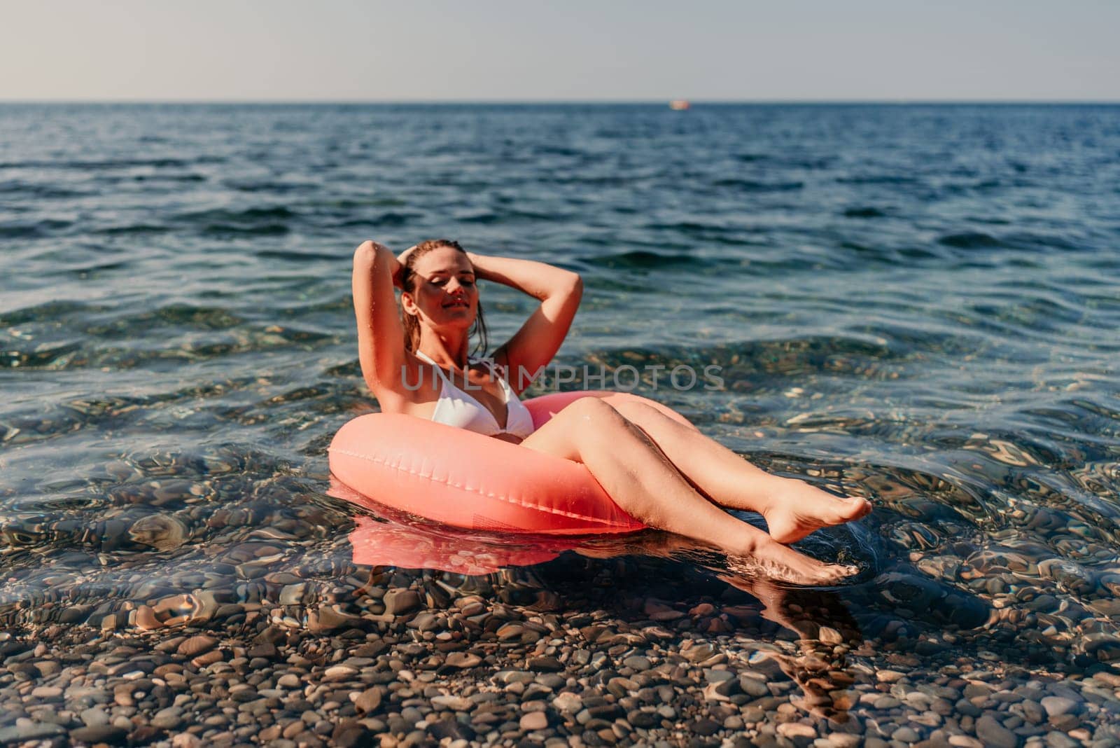 A woman is floating on a red inflatable tube in the ocean. She is smiling and enjoying the water