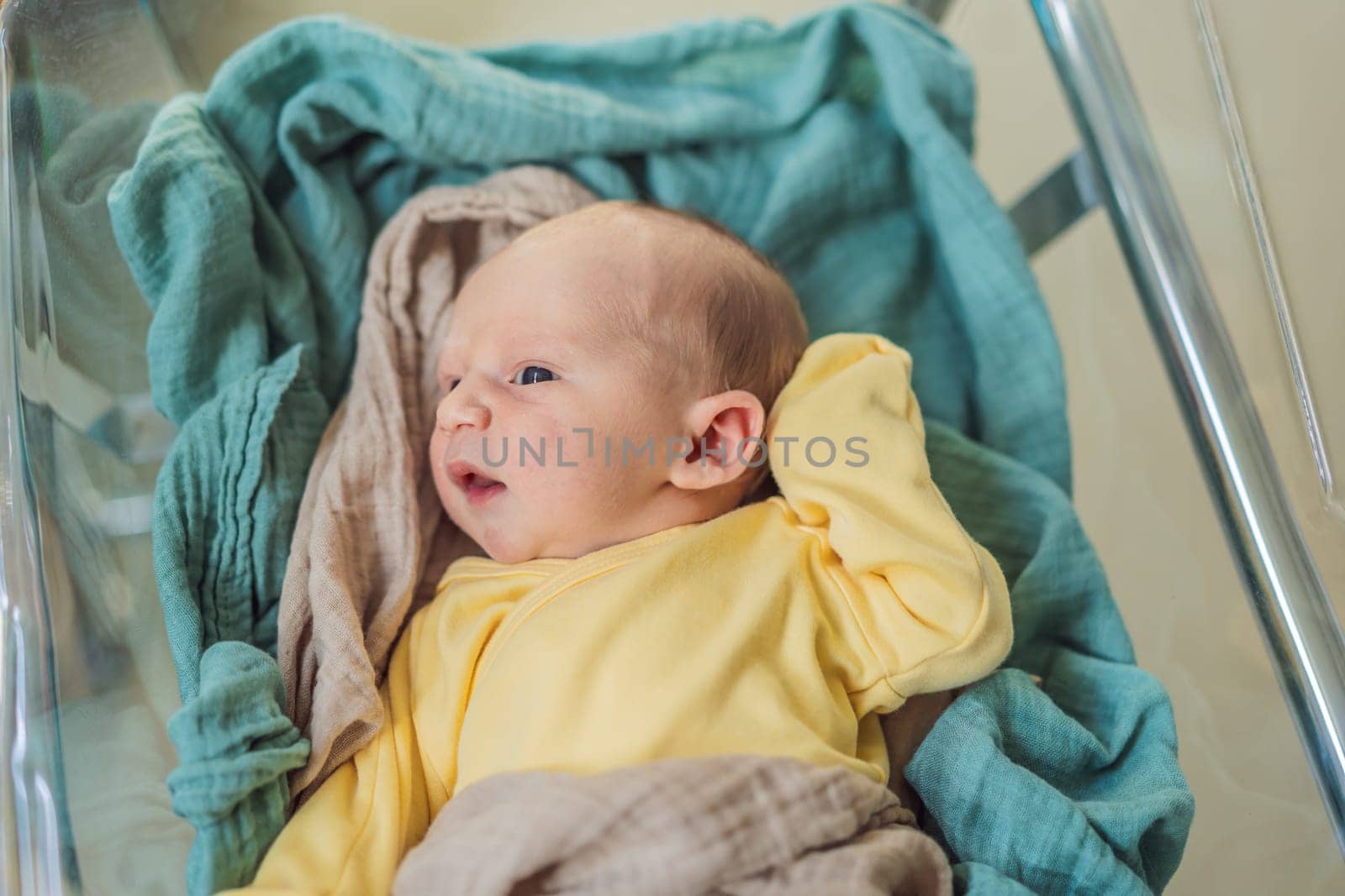 A newborn rests peacefully in his transparent bassinet in the hospital. The clear bassinet provides visibility for medical staff to monitor the baby's well-being while ensuring a safe and comfortable environment for the newborn.