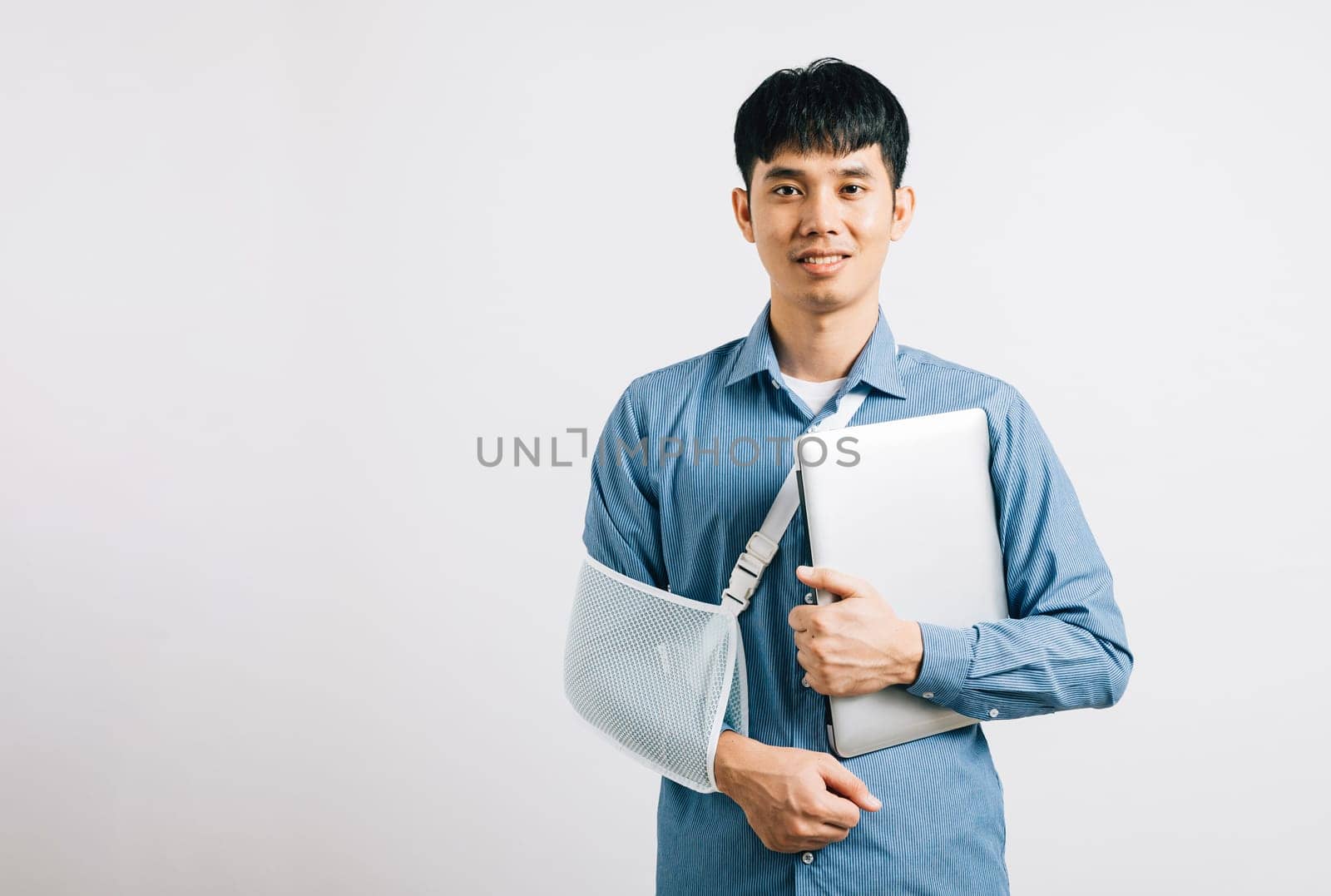 Confident Asian businessperson, with a broken arm, carries on working with a laptop, supported by a splint. Studio shot isolated on white, emphasizing determination and recovery. Copy space is offered