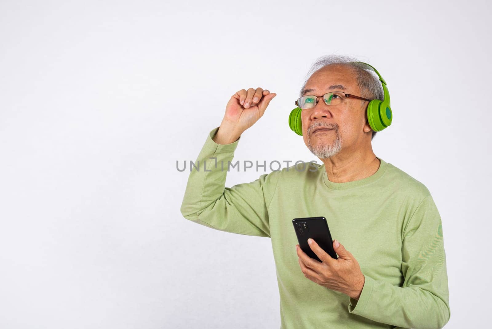 Portrait Asian smiling old man headphones is holding smartphone listen music in headphones and dancing studio shot isolated on white background, Funny senior by Sorapop
