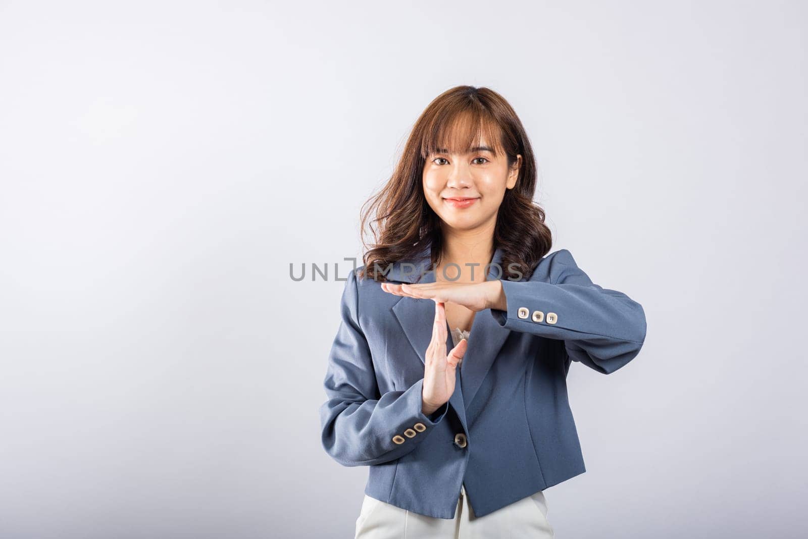 Closeup portrait young business woman wearing a suit smiling making time out gesture with hands studio shot isolated on white background, demonstrates break hand sign, stop time by Sorapop