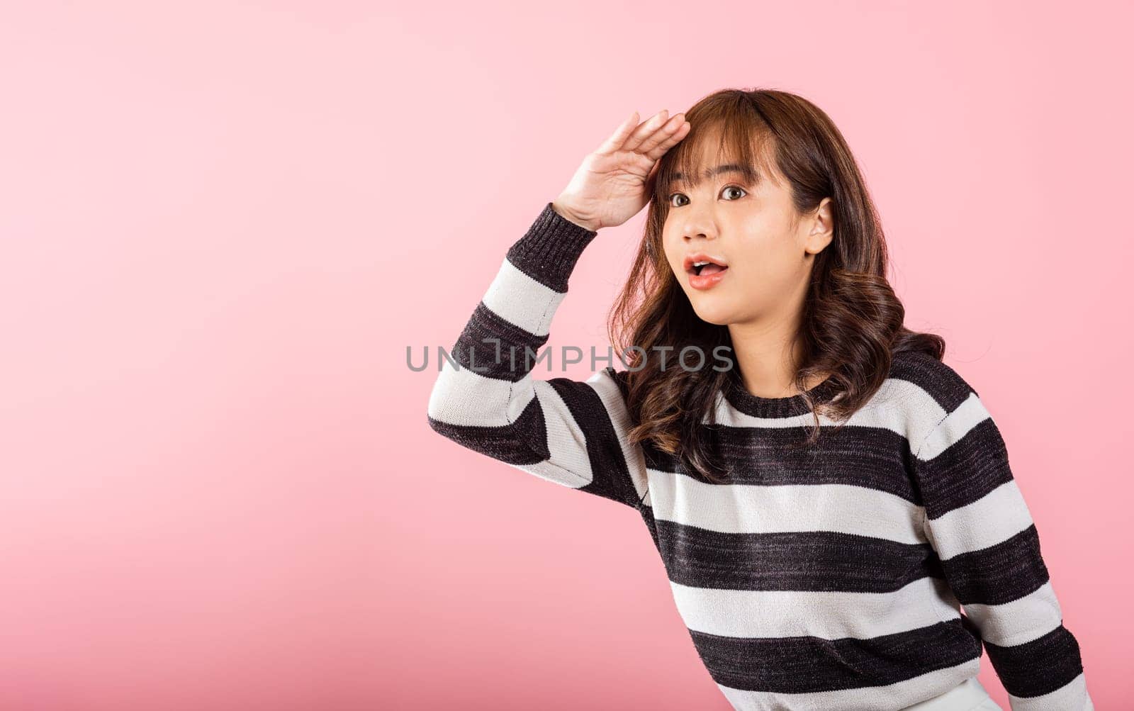 Searching concept. Asian woman looking far away with hand over head at studio shot isolated on pink background, Portrait of Happy female looking at distance with eyes shaded, copy space. by Sorapop