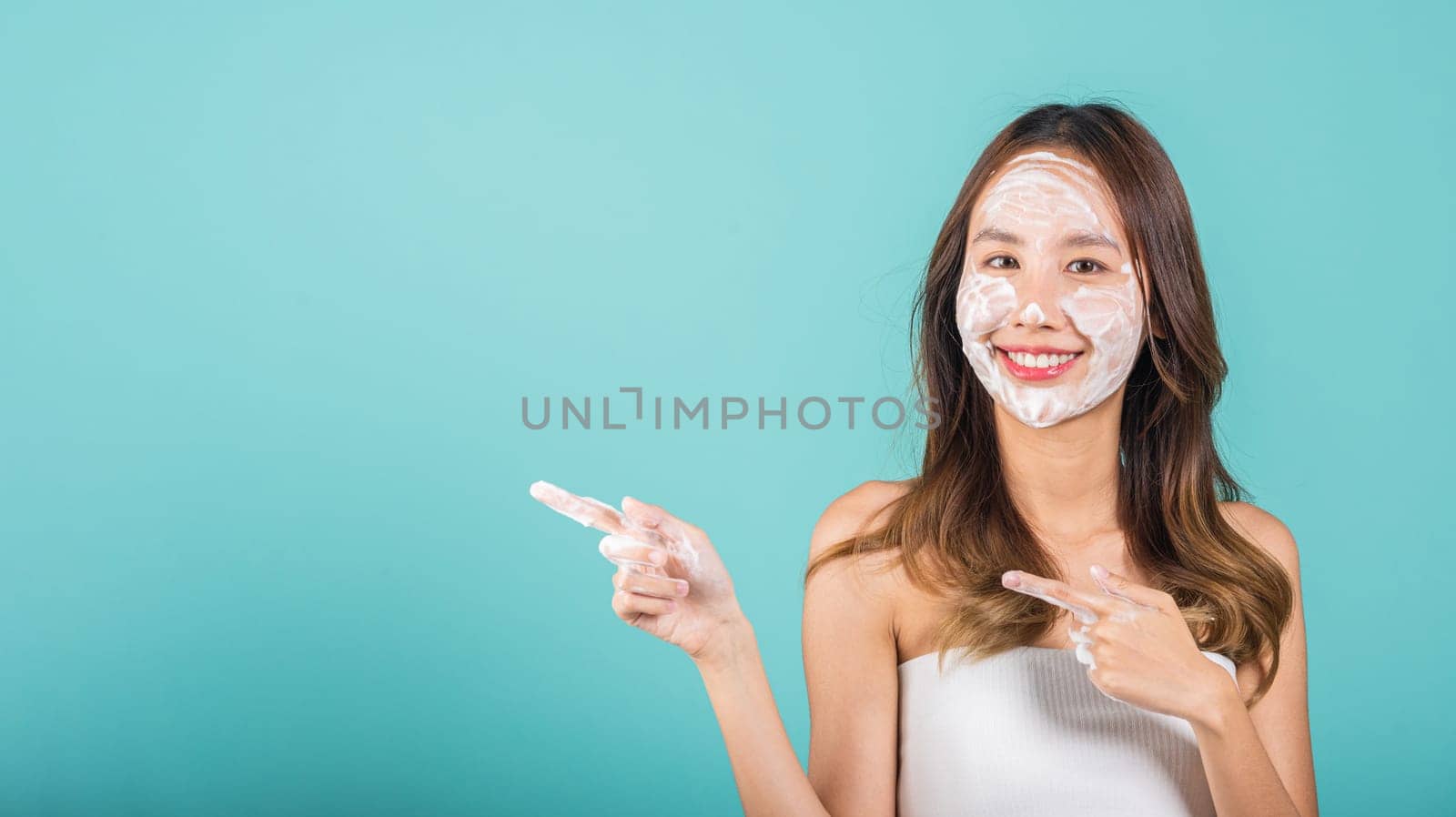 Portrait Asian woman washing face foaming facewash soap scrub on skin studio shot isolated on blue background, beautiful female applying bubble facial foam and cleansing by Sorapop
