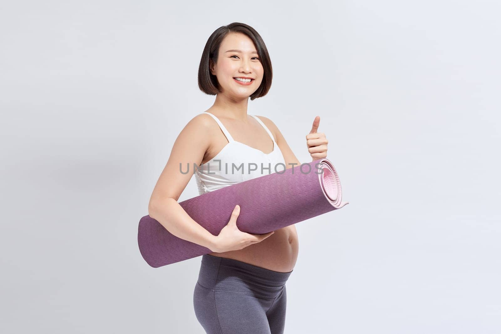 Portrait of a young pregnant woman holding a yoga mat in the studio on a white background