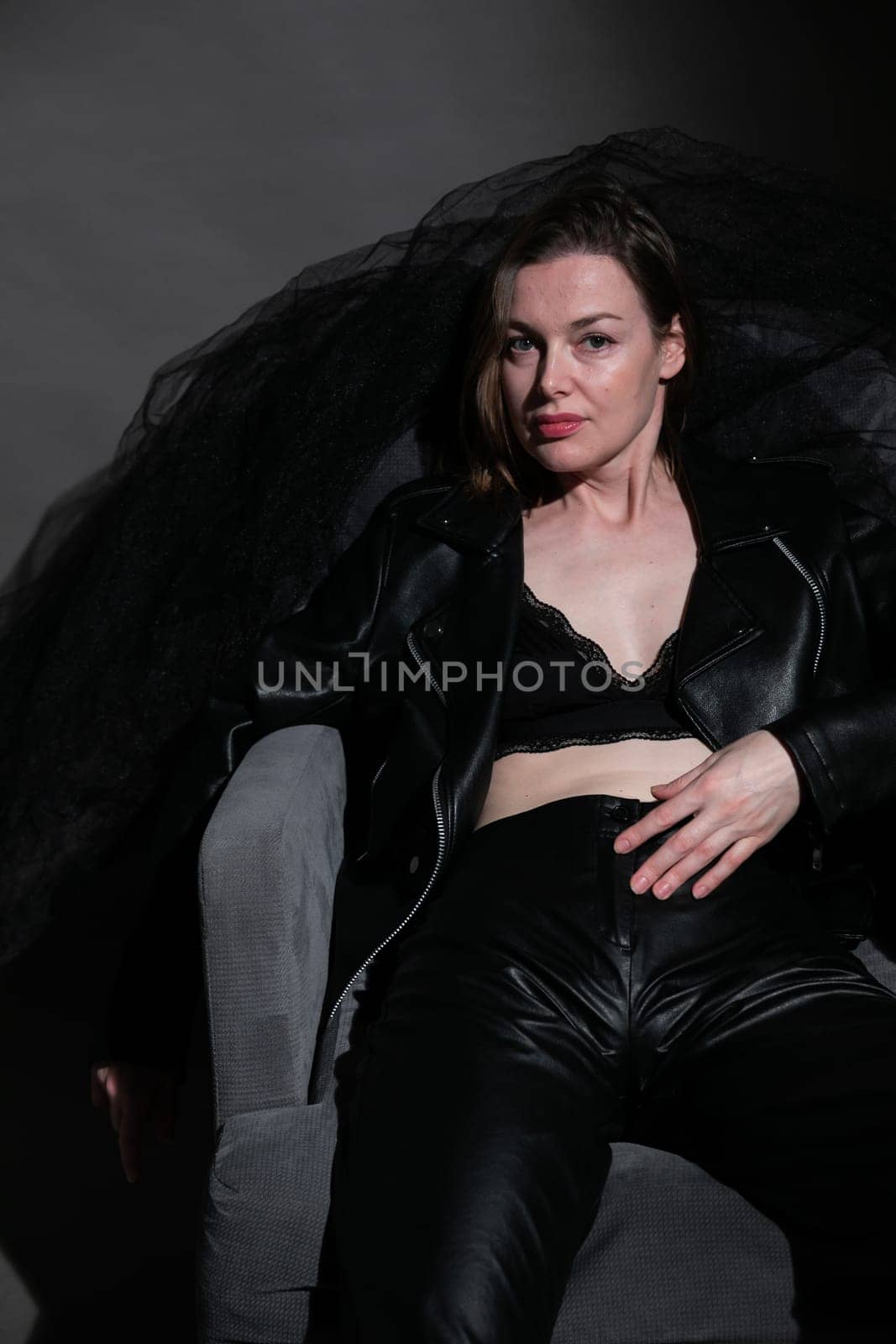 woman in dark clothes and a bra sits on a chair in a dark room