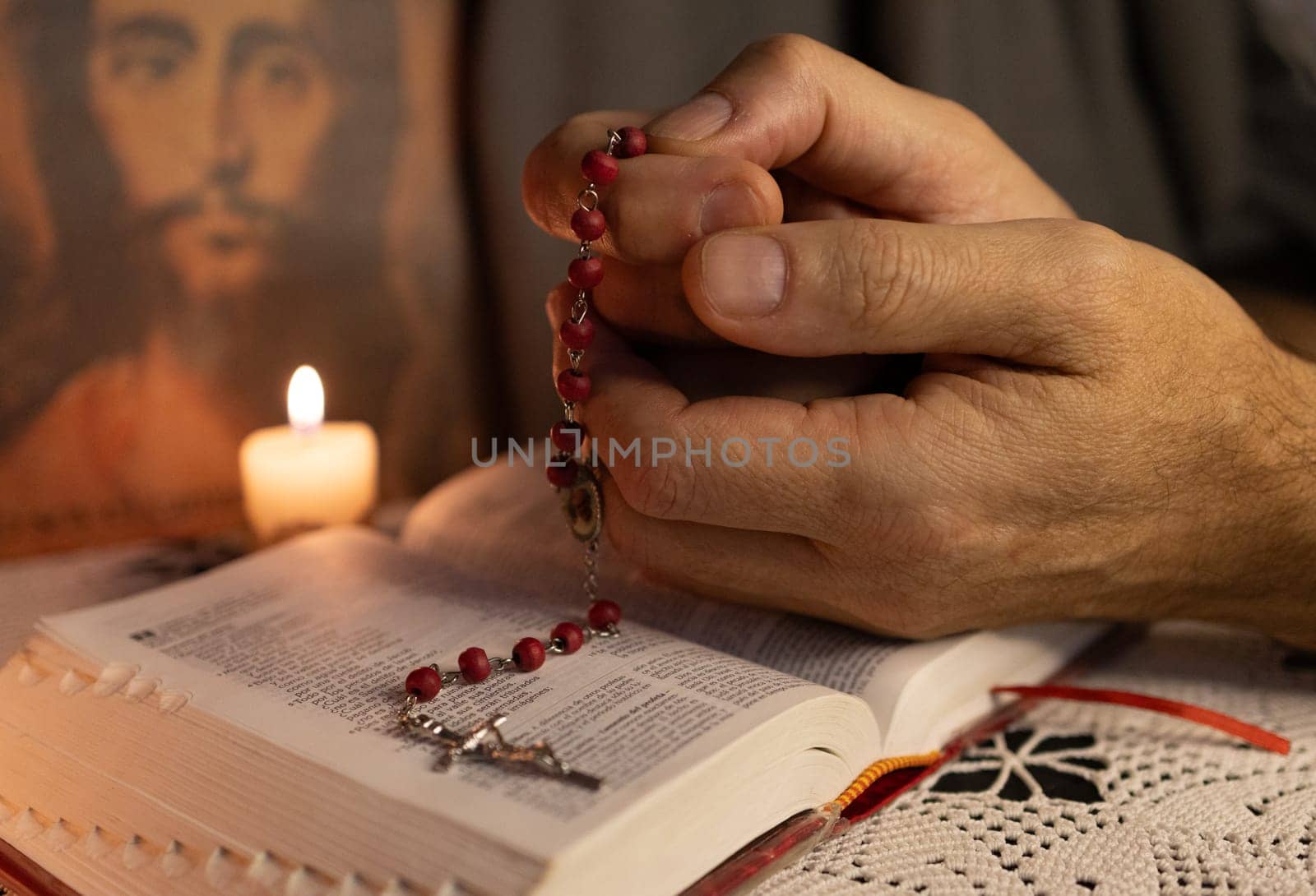 Hands of a young man praying the rosary..Jesus face in the blurred background. by VeroDibe