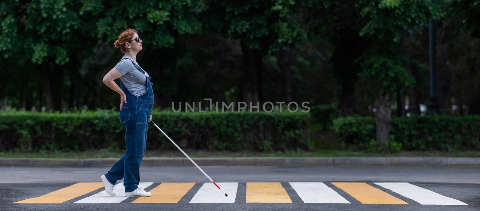 Blind pregnant woman crosses the road at a crosswalk with a cane. by mrwed54