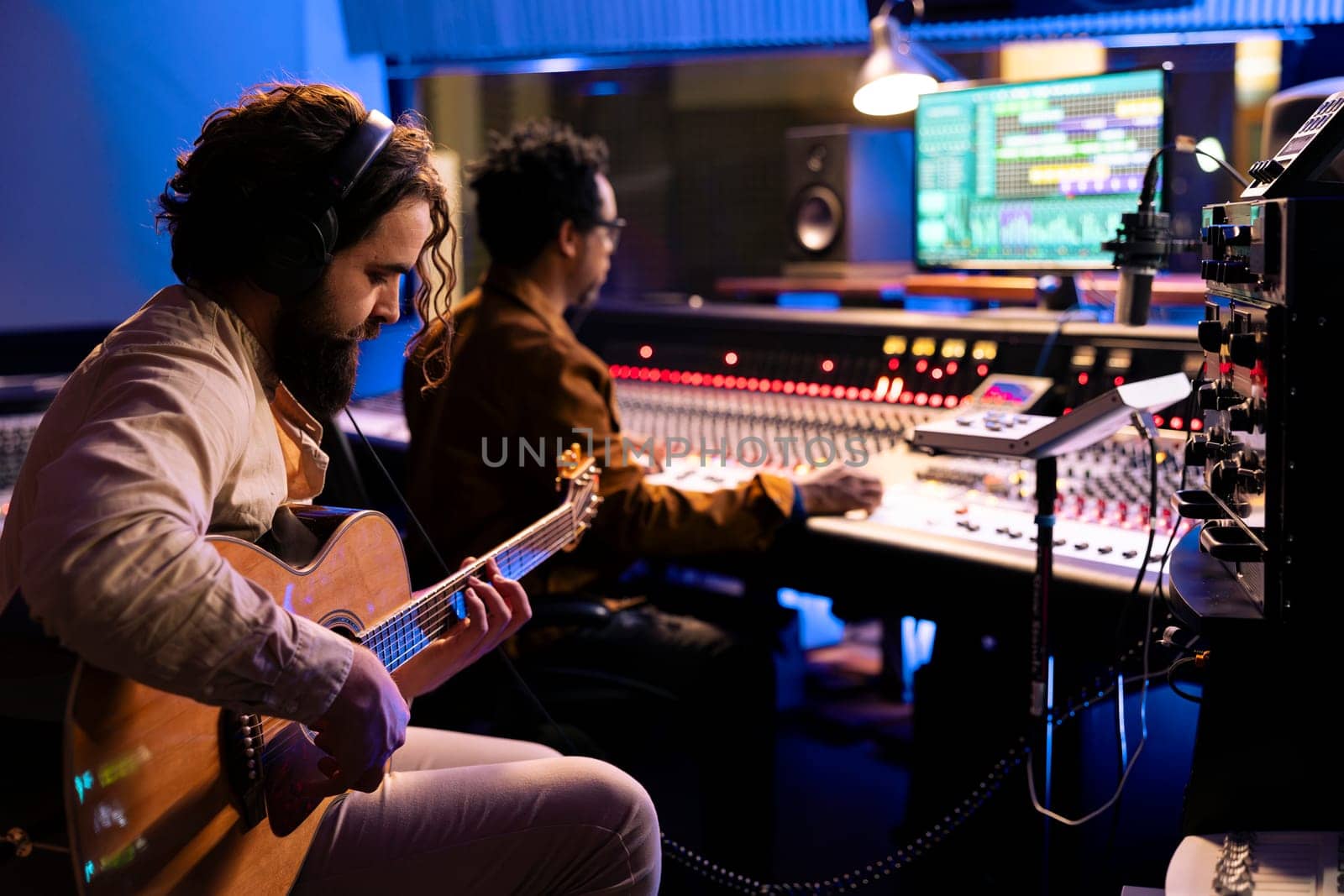 Skilled artist musician recording his guitar sounds in professional studio, using electro acoustic tunes to edit another record for an album. Singer composing music with audio expert in control room.