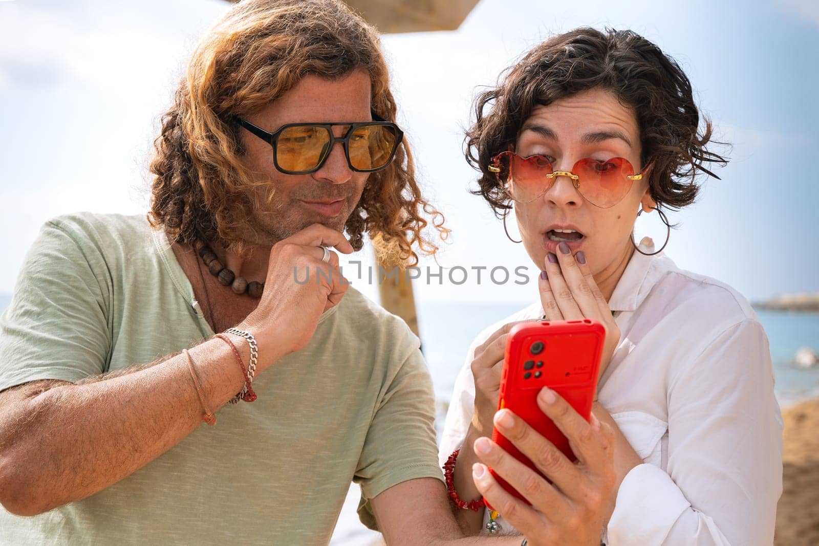 Smiling couple on the beach browsing smartphone apps. by mariaphoto3