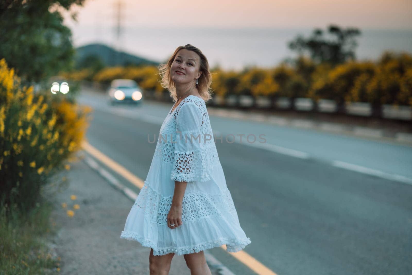 A woman in a white dress is standing on the side of a road by Matiunina