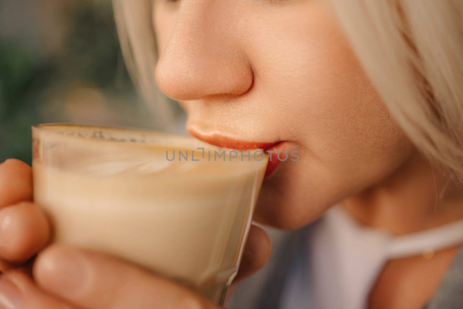 A blonde woman is drinking coffee from a glass. She is smiling and she is enjoying her drink. by Matiunina