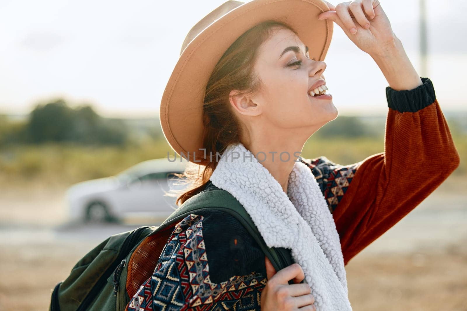 Woman in stylish hat and cozy sweater gazes at sky with vintage car in background on sunny day