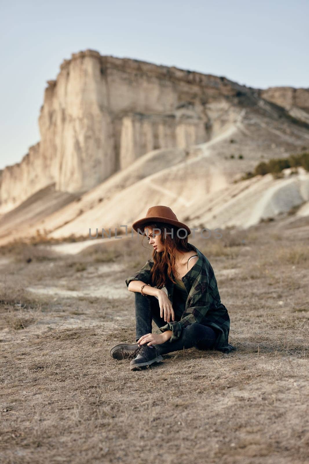 Woman wearing hat sitting in front of majestic mountain peak