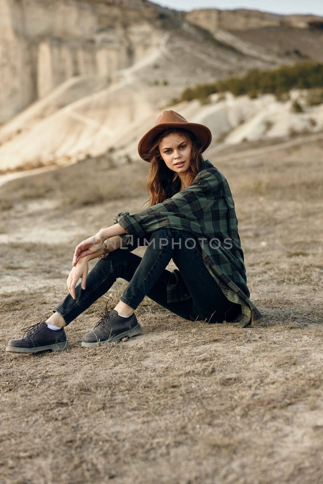 serene young woman in hat sitting amidst desert landscape with majestic mountains in the background by Vichizh