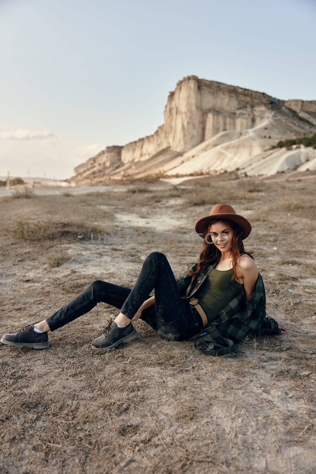 Serene woman in hat sitting crosslegged in front of majestic mountain peak