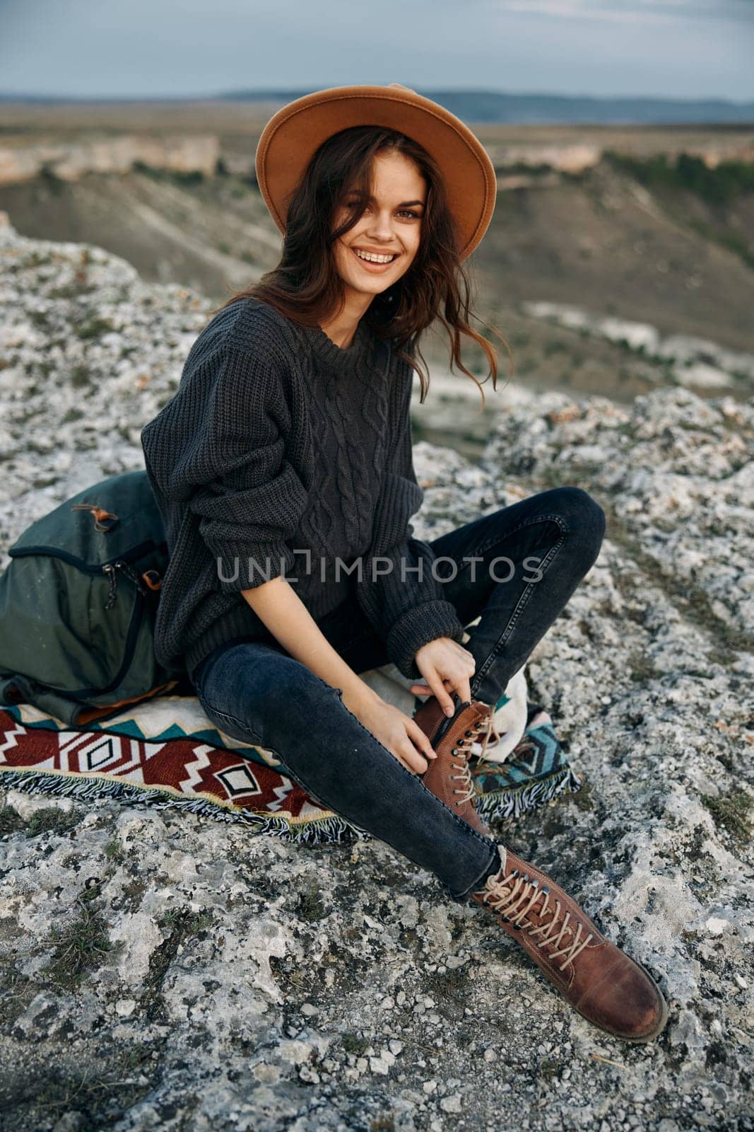 Serene woman in hat and boots sitting on rock rug in tranquil nature setting by Vichizh