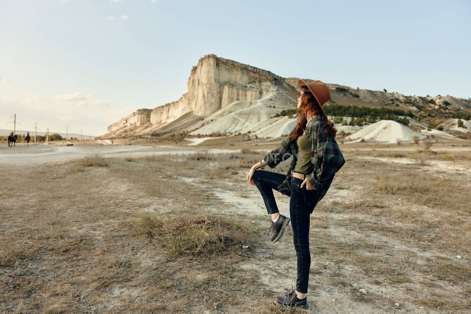 Confident woman standing with hands on hips in front of majestic mountain scenery by Vichizh