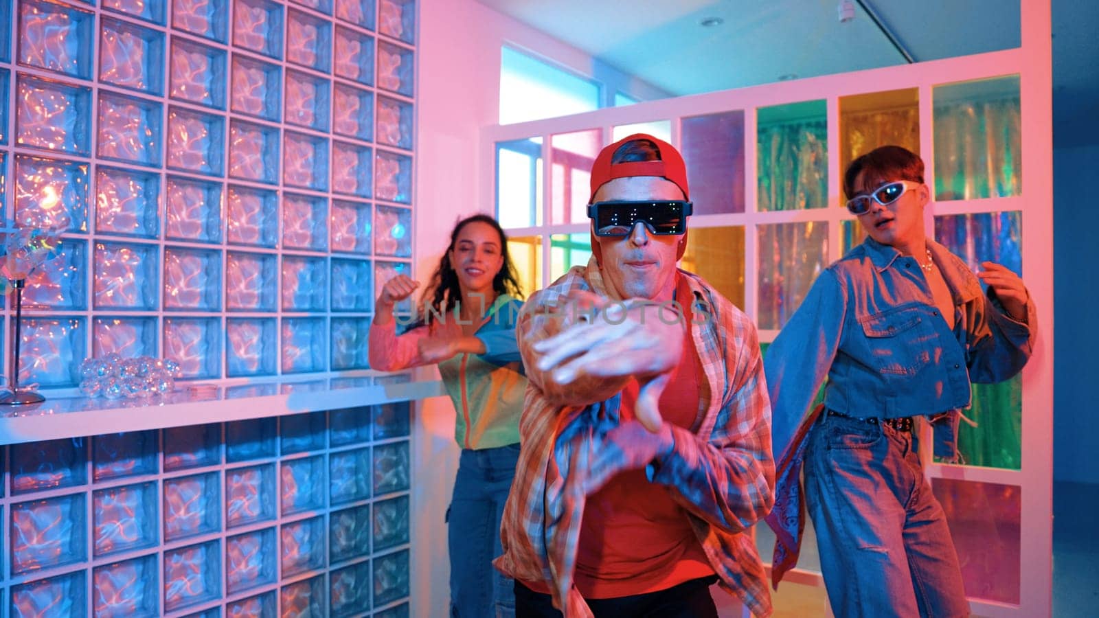 Handsome hipster wearing fancy glasses while dancing with diverse team moving along freestyle music with happiness. Caucasian hipster perform street dancing in bright neon light at club. Regalement.