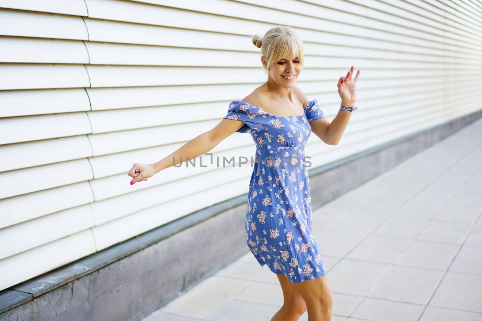 Sensual blonde woman in summer dress dancing happily modern music in the city