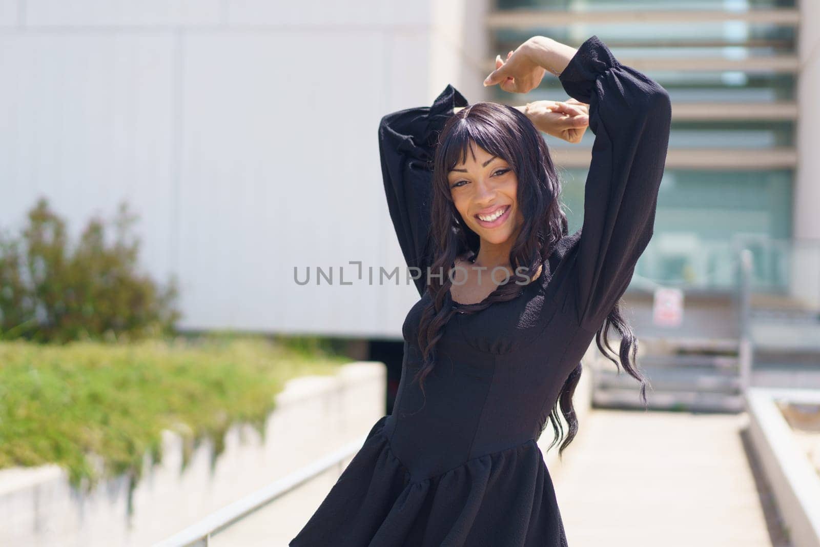 Energetic caucasuan young woman smiling at camera while dancing in the city wearing summer black dress