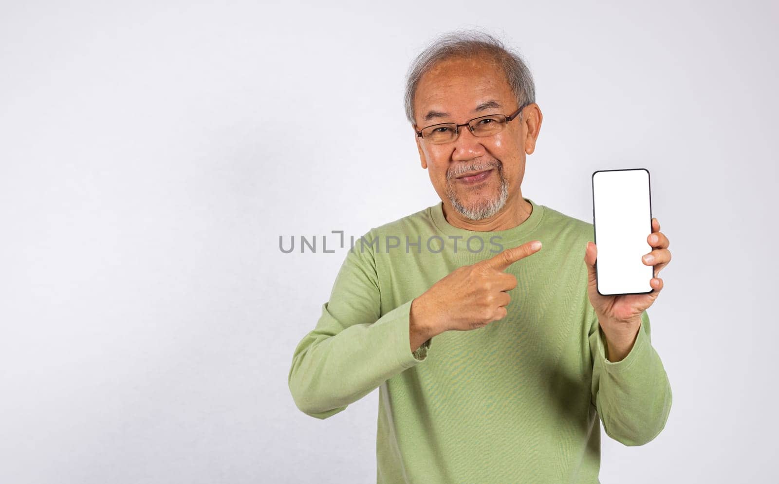 Portrait Asian smiling old man holding a cell phone and pointing to blank screen studio shot isolated on white background by Sorapop