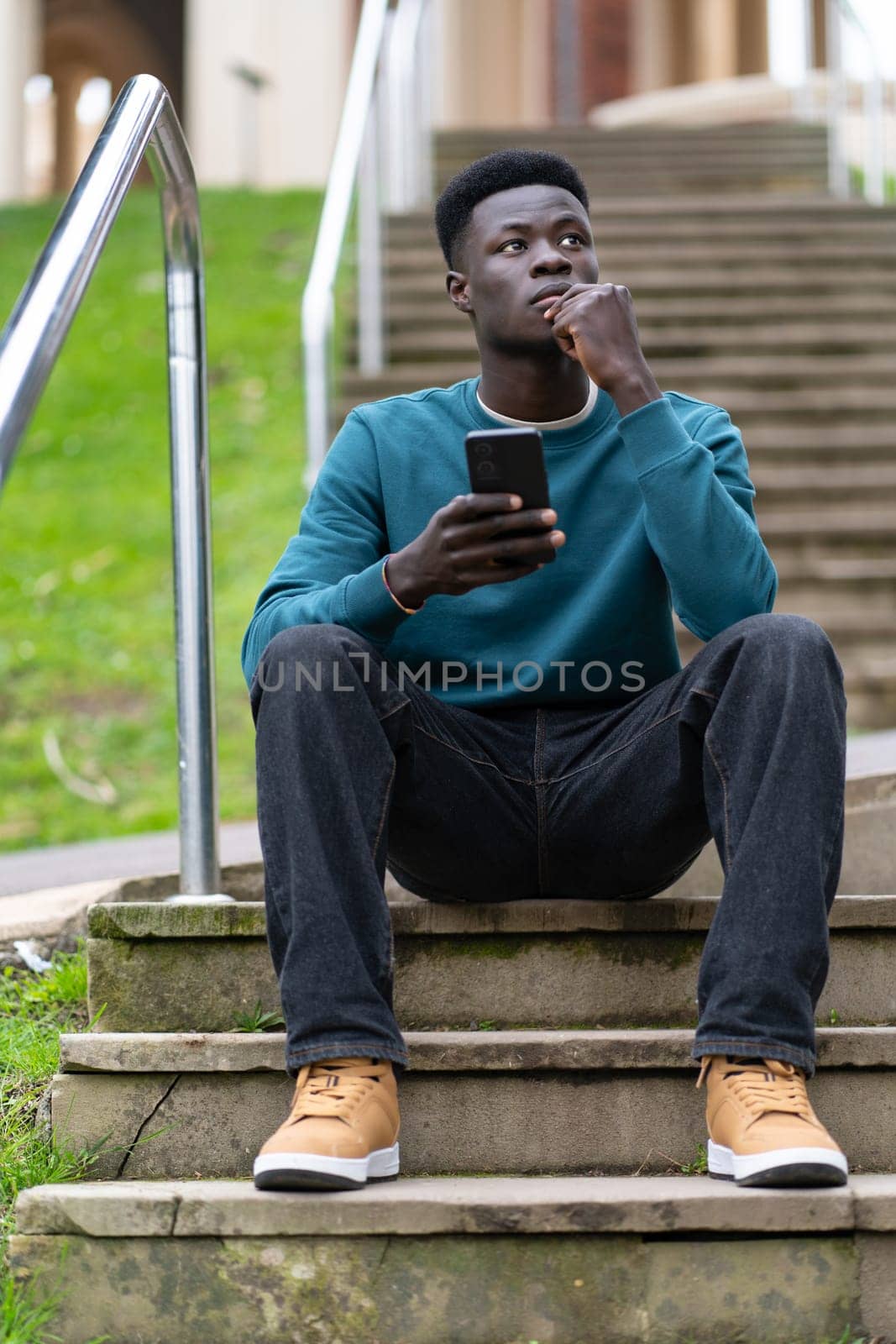 A young man sits on a set of stairs with his cell phone in his hand. He is deep in thought, possibly contemplating something important
