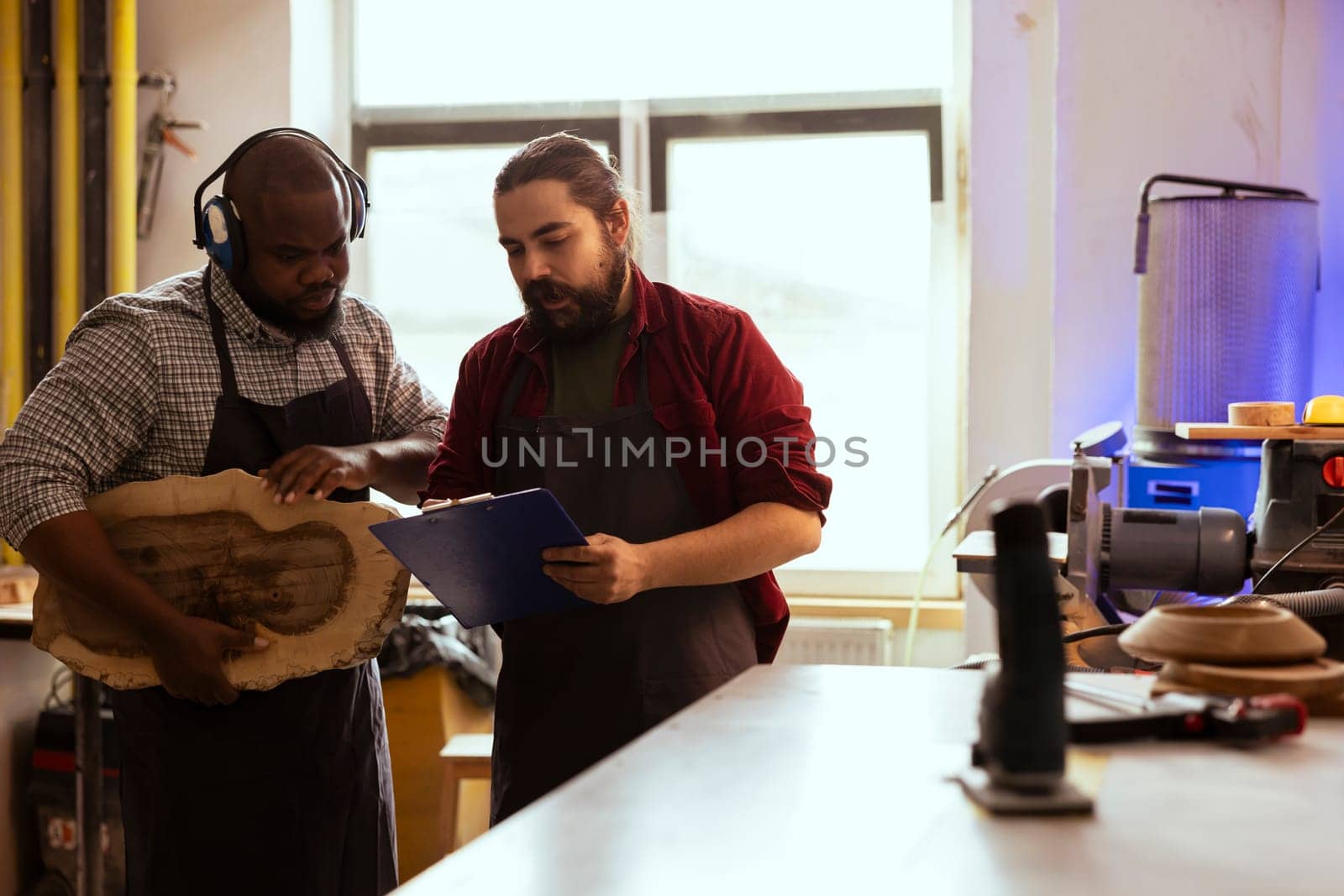 Cabinetmaker and apprentice looking over technical drawings on notepad to make creative wood art pieces. Artisan and BIPOC colleague looking at blueprints to execute woodworking projects