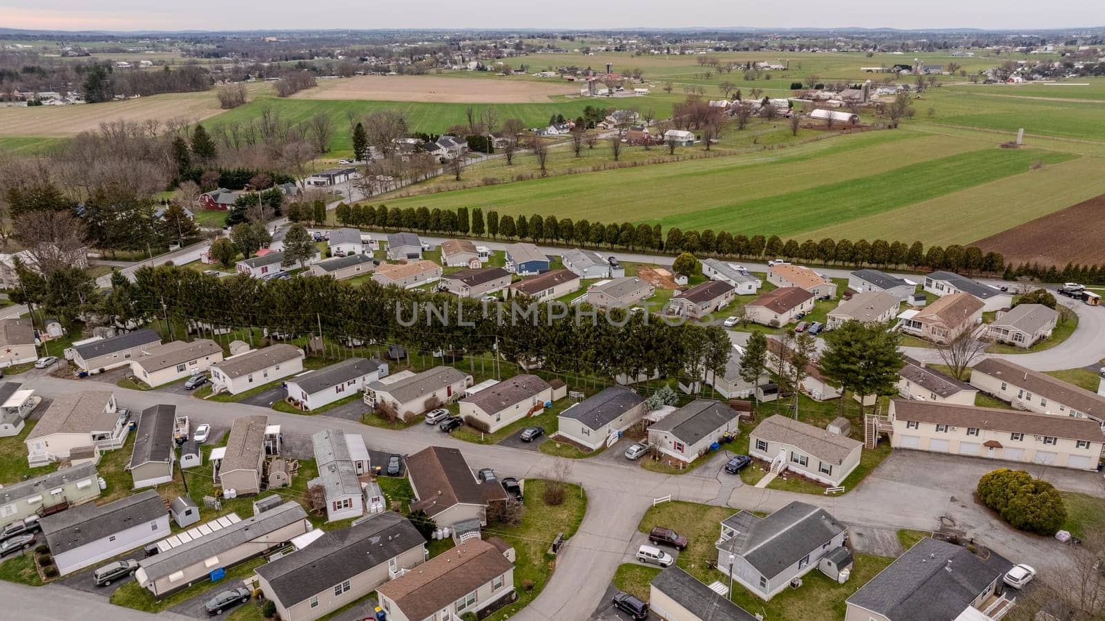 Aerial View Of A Compact Suburban Neighborhood With Rows Of Mobile, Manufactured, Prefab, Homes And Small Houses, Nestled Among Open Fields And Trees, Highlight