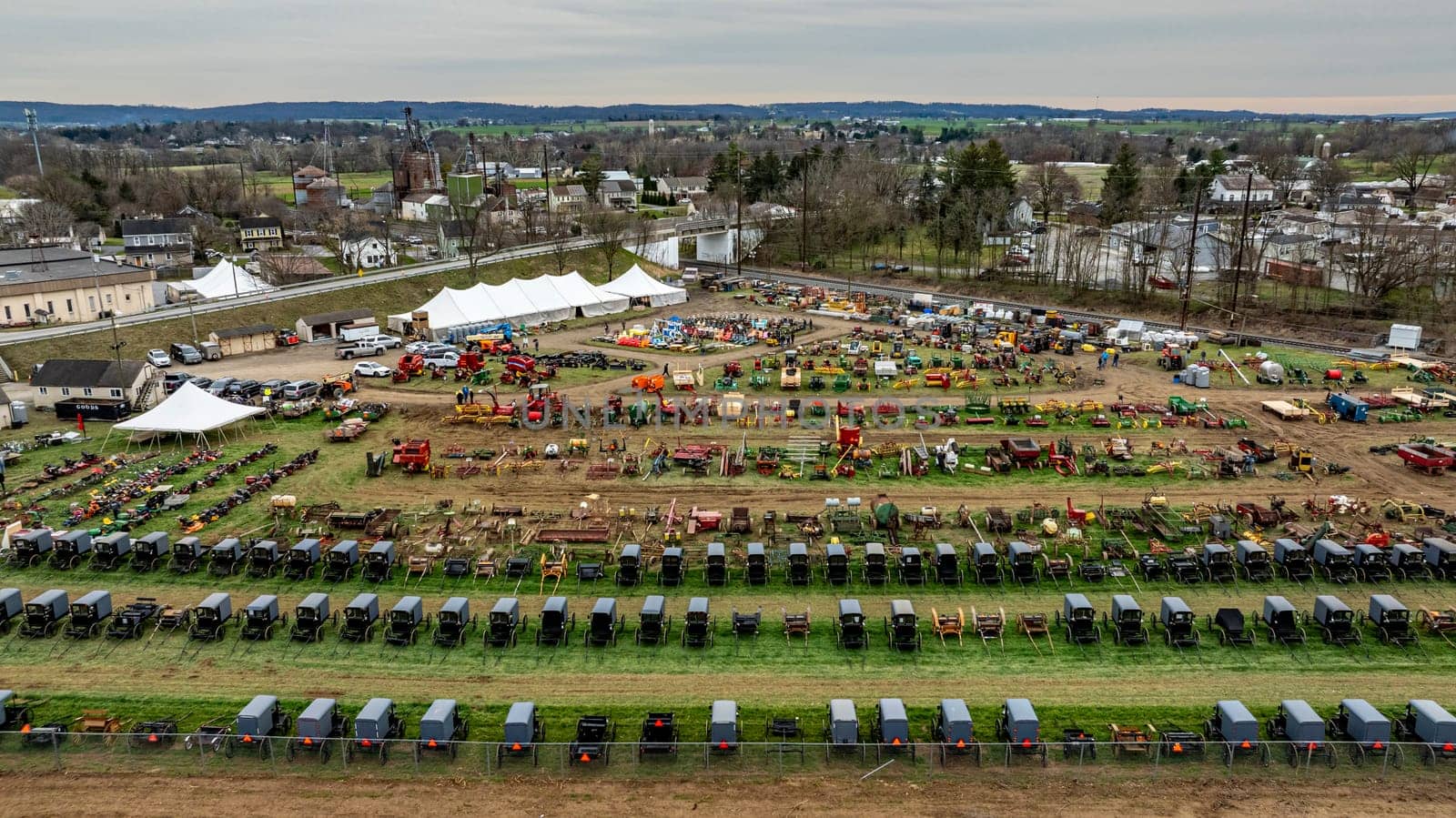 Gordonville, Pennsylvania, USA, March 3, 2024 - A bustling rural auction comes to life in this overhead shot, capturing rows of Amish buggies and an array of agricultural equipment on sale.