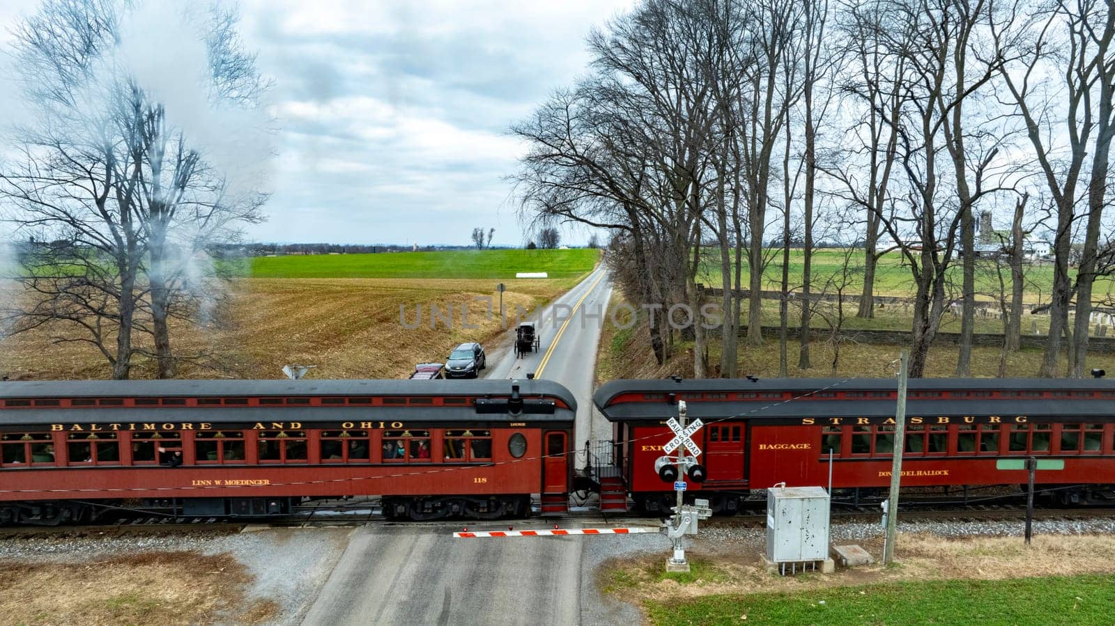 Ronks, Pennsylvania, USA, December 30, 2023 - A Historic Train Crossing Rural Road with an Amish Horse-Drawn Carriage