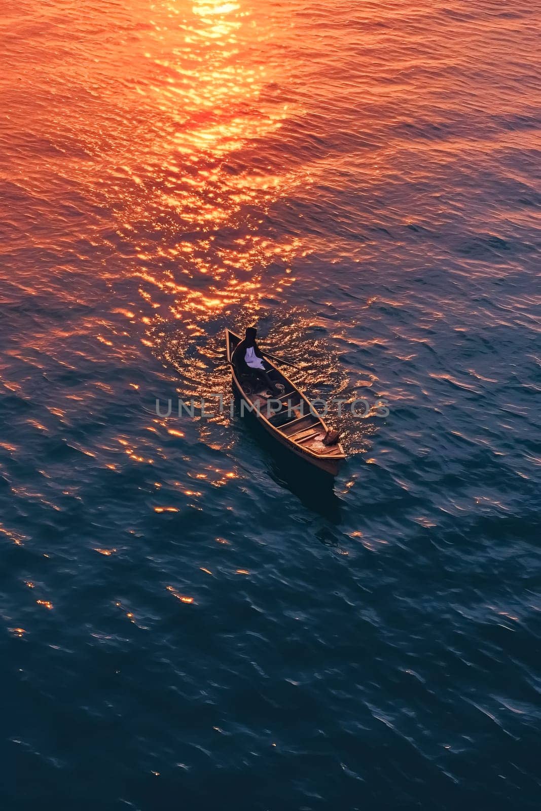 A man is in a canoe on a lake at sunset. The sky is orange and the water is calm