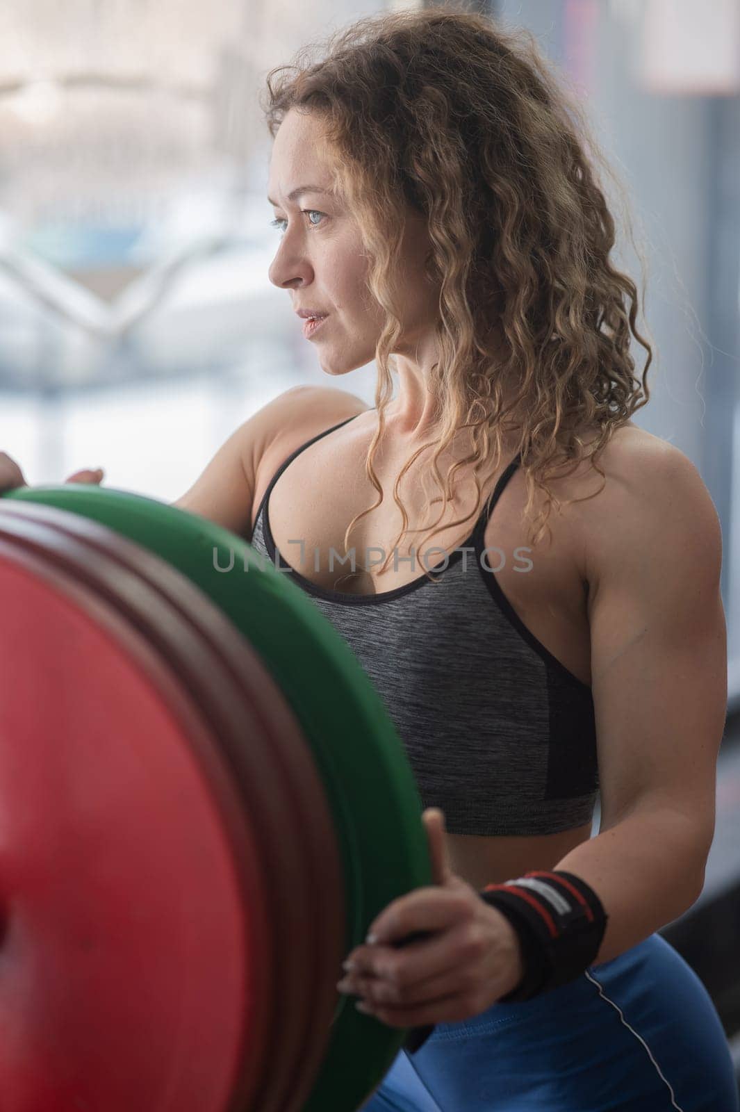 Caucasian forty year old woman putting a weight plate on a barbell in the gym. Vertical photo