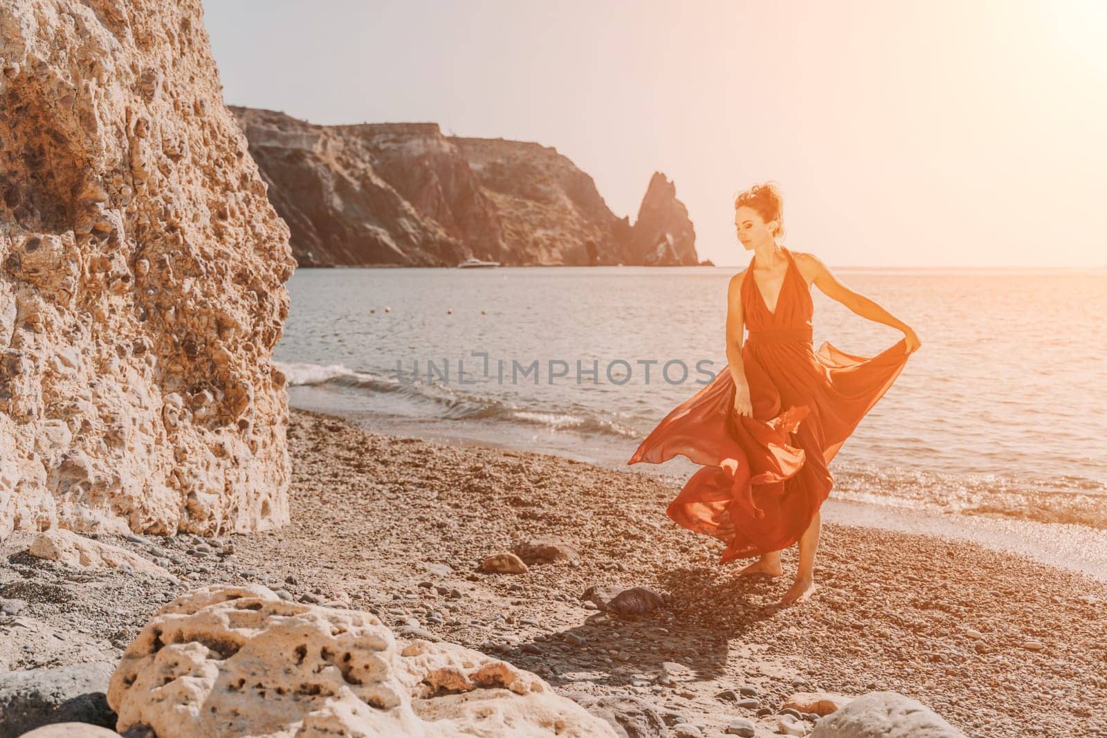 Woman red dress sea. Female dancer in a long red dress posing on a beach with rocks on sunny day. Girl on the nature on blue sky background. by Matiunina