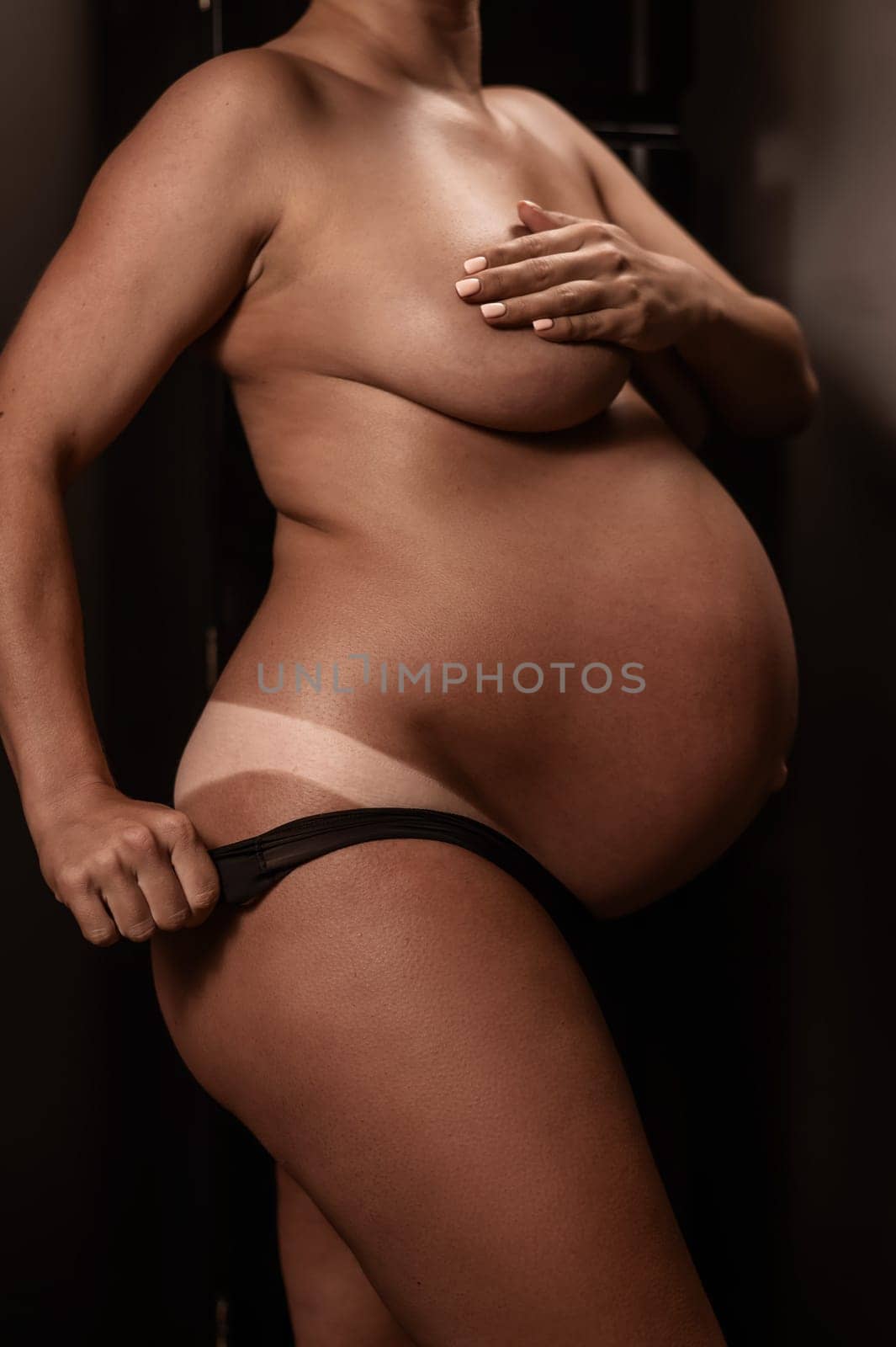 Pregnant woman pulls back her panties showing instant tan. Vertical photo