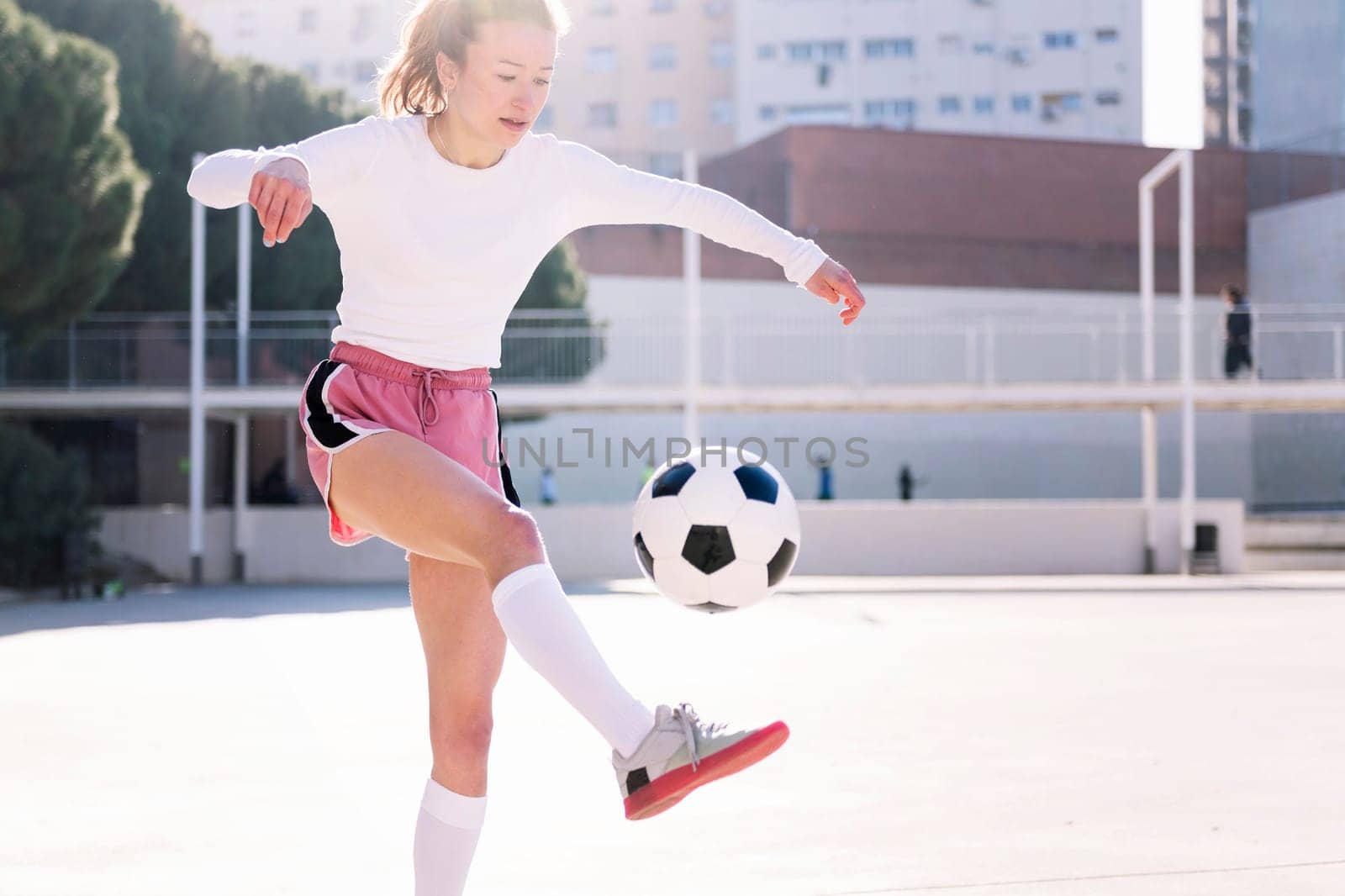 female soccer player kicking the ball with her feet on an urban football court, concept of sport and active lifestyle